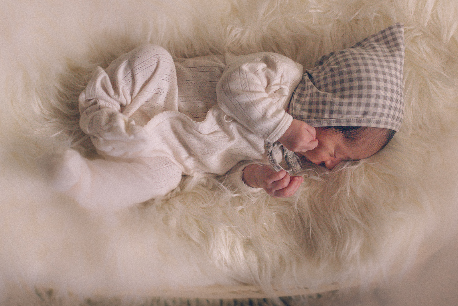 A look down at a sleeping newborn in a white onesie and bonnet on a fur blanket after exploring Forever French