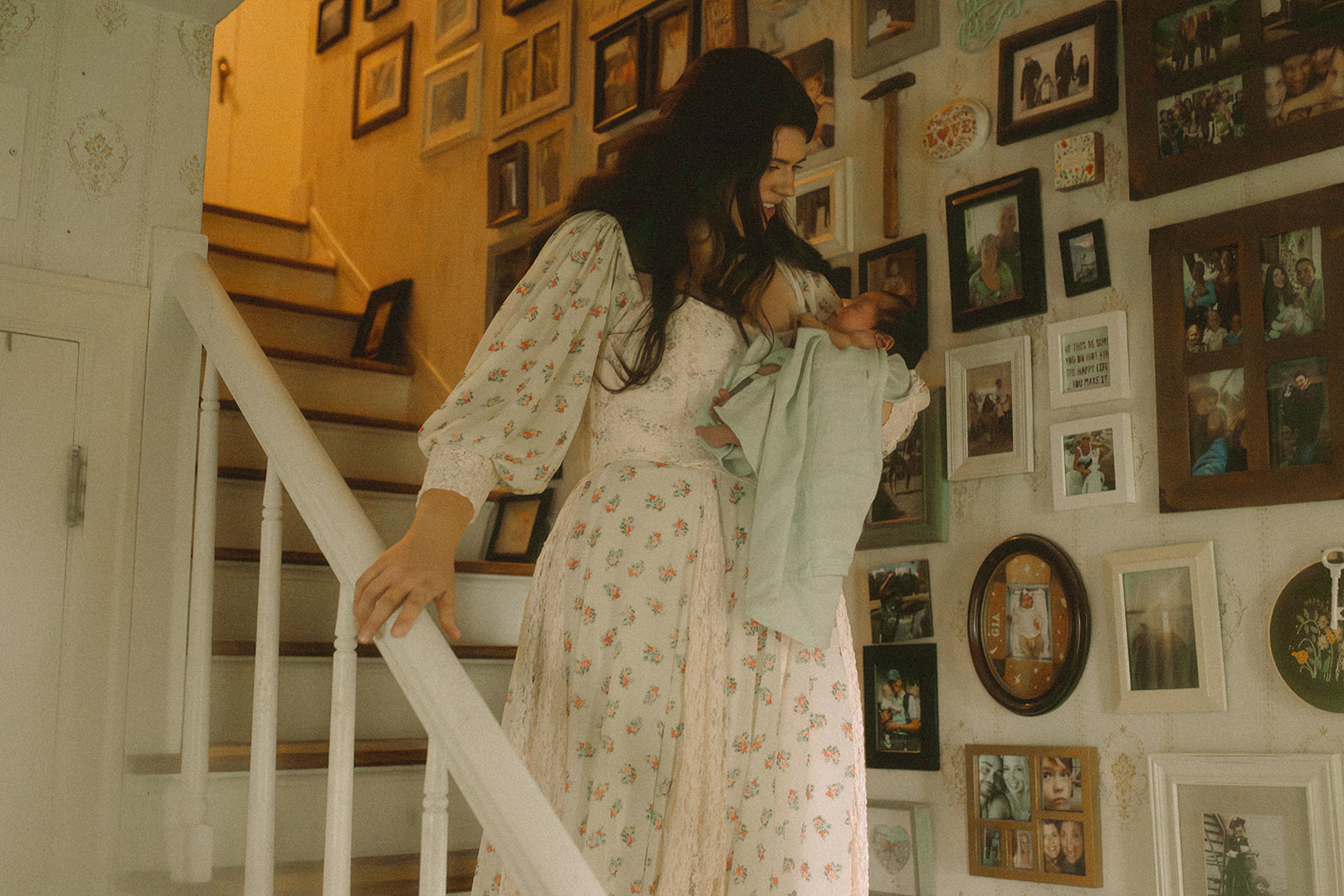 A happy mom in a flower print dress walks down the stairs covered in pictures with her newborn after visiting Forever French