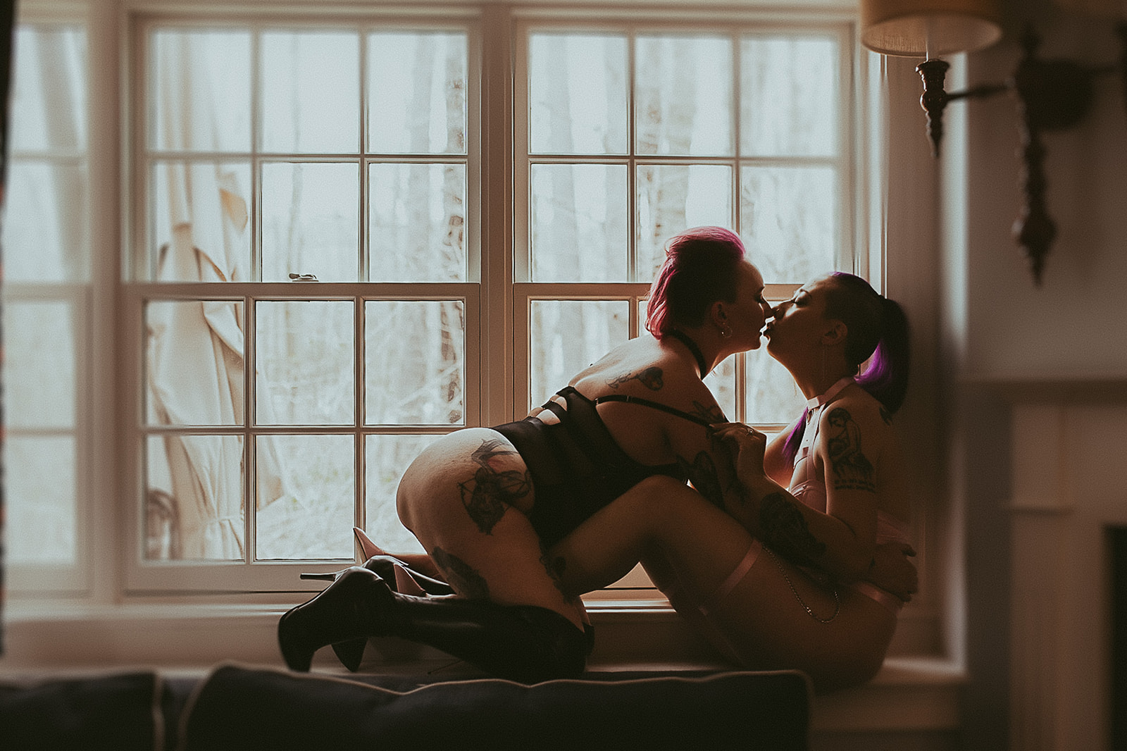 Two tattooed women in lingerie lean in for a kiss in a window sill after getting color at hair salons in MIssoula
