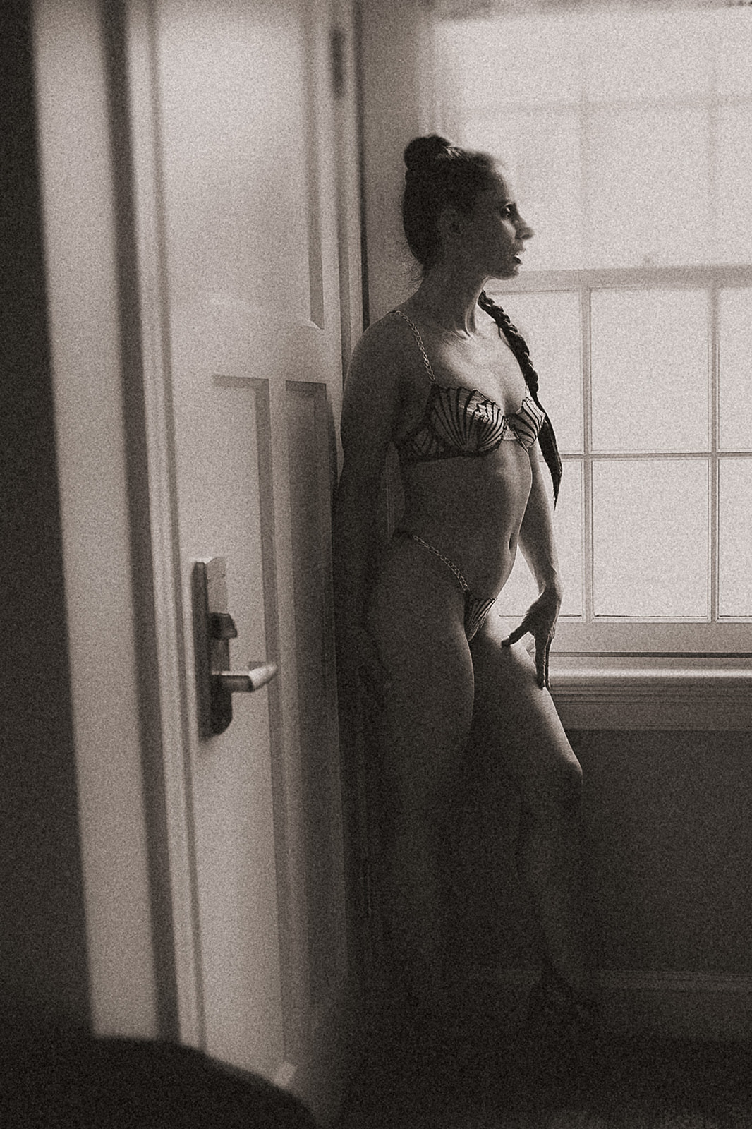 A woman in lingerie stands in a window in heels looking out