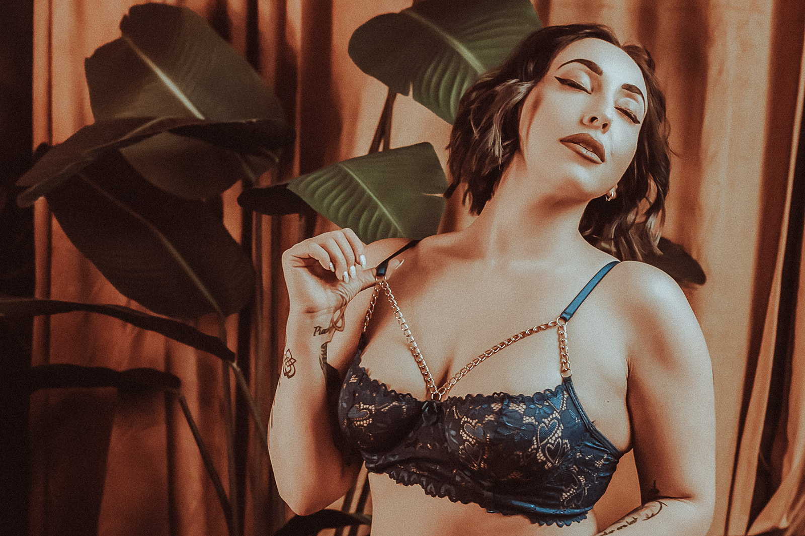A woman pulls on her bra strap of black lace lingerie in a studio