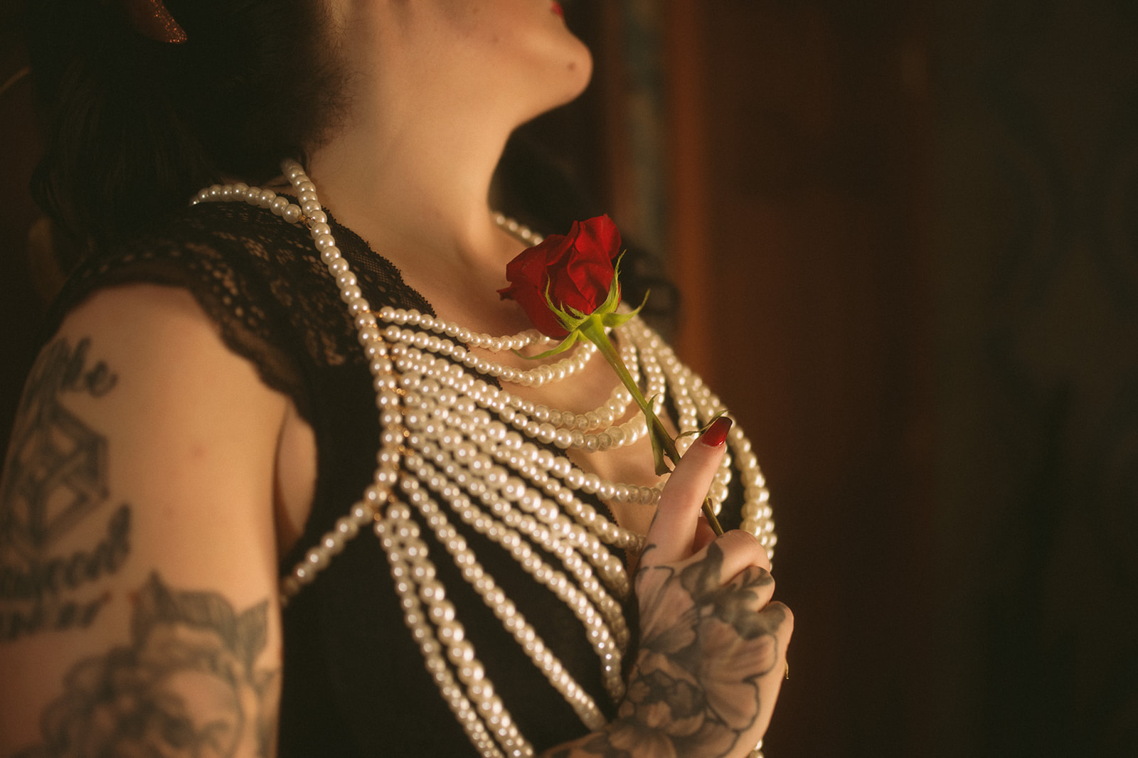 A woman with tattoos holds a red rose against her chest covered in pearls after visiting nail salons in Bozeman